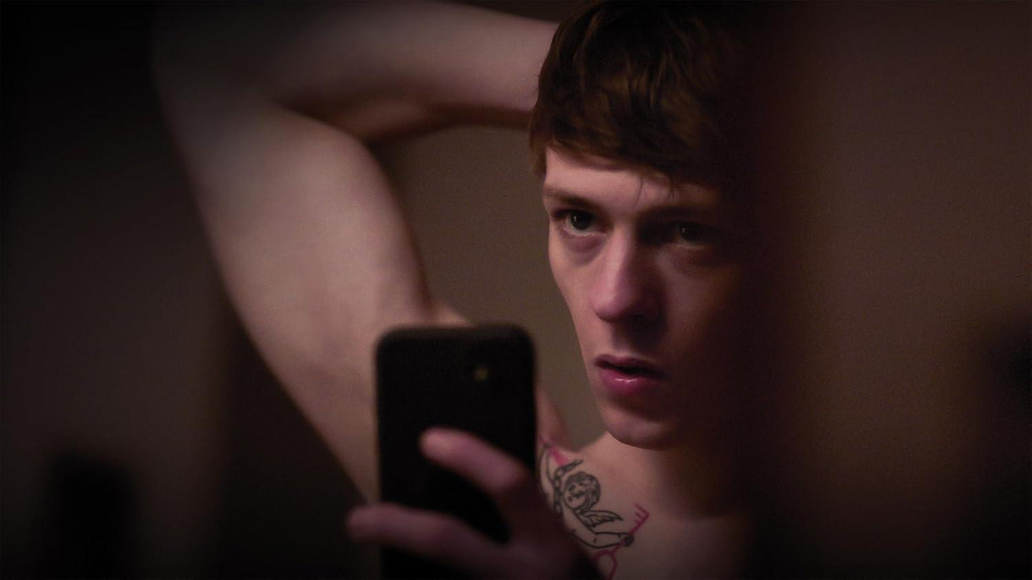 Ein Mann mit Tattoo macht ein Selfie im Spiegel.