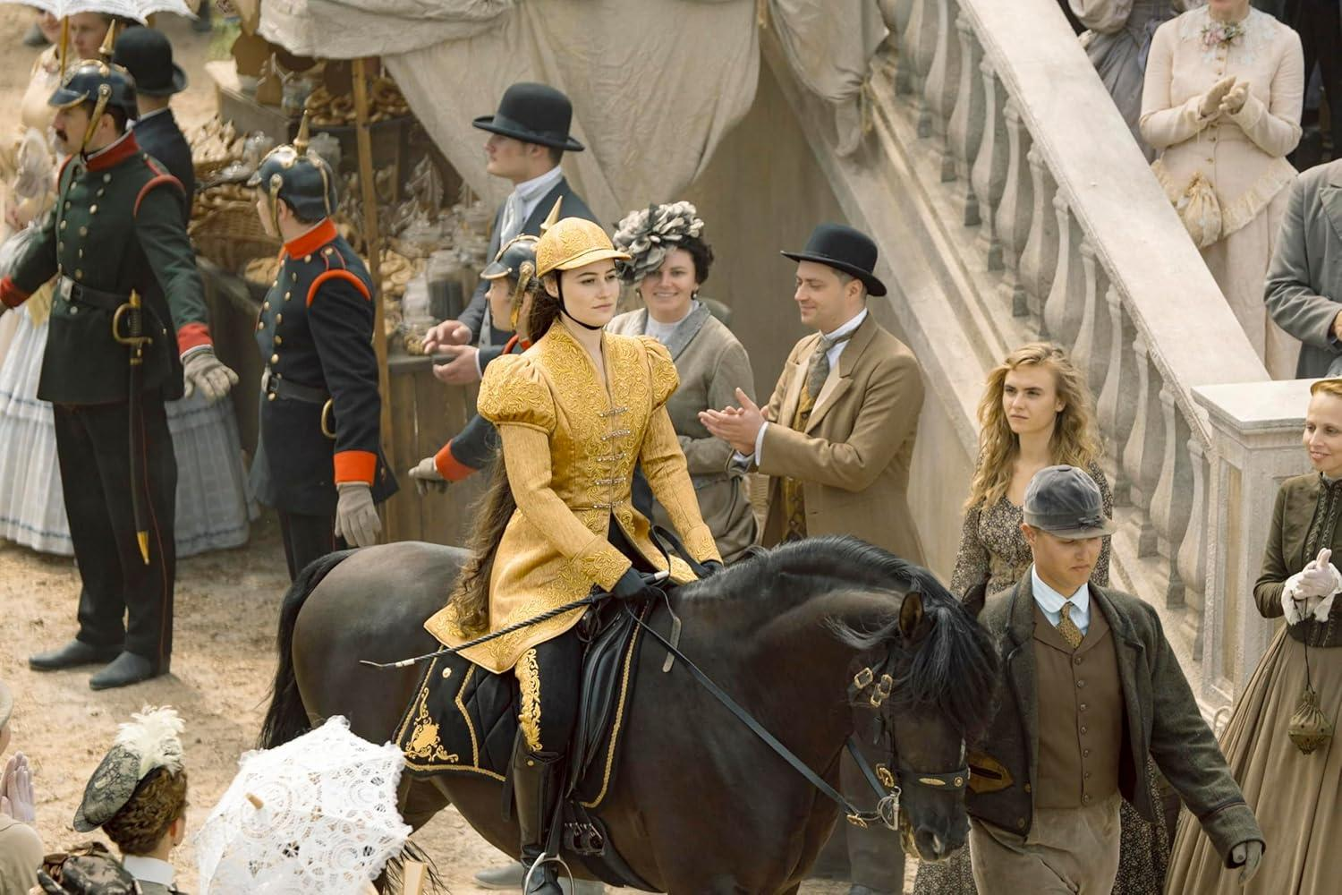 Reiterin in goldener Kleidung auf einem Pferd, umgeben von Menschen in historischer Kleidung.
