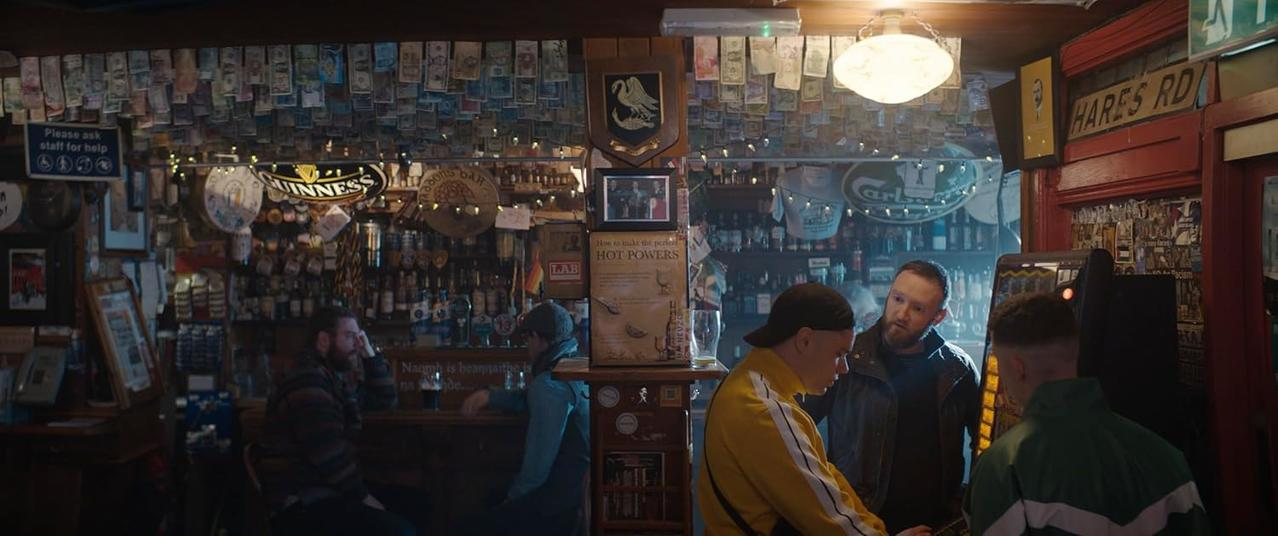 Männer in einer Bar, Geld an der Decke, Guinness-Schilder und Flaschenregale.
