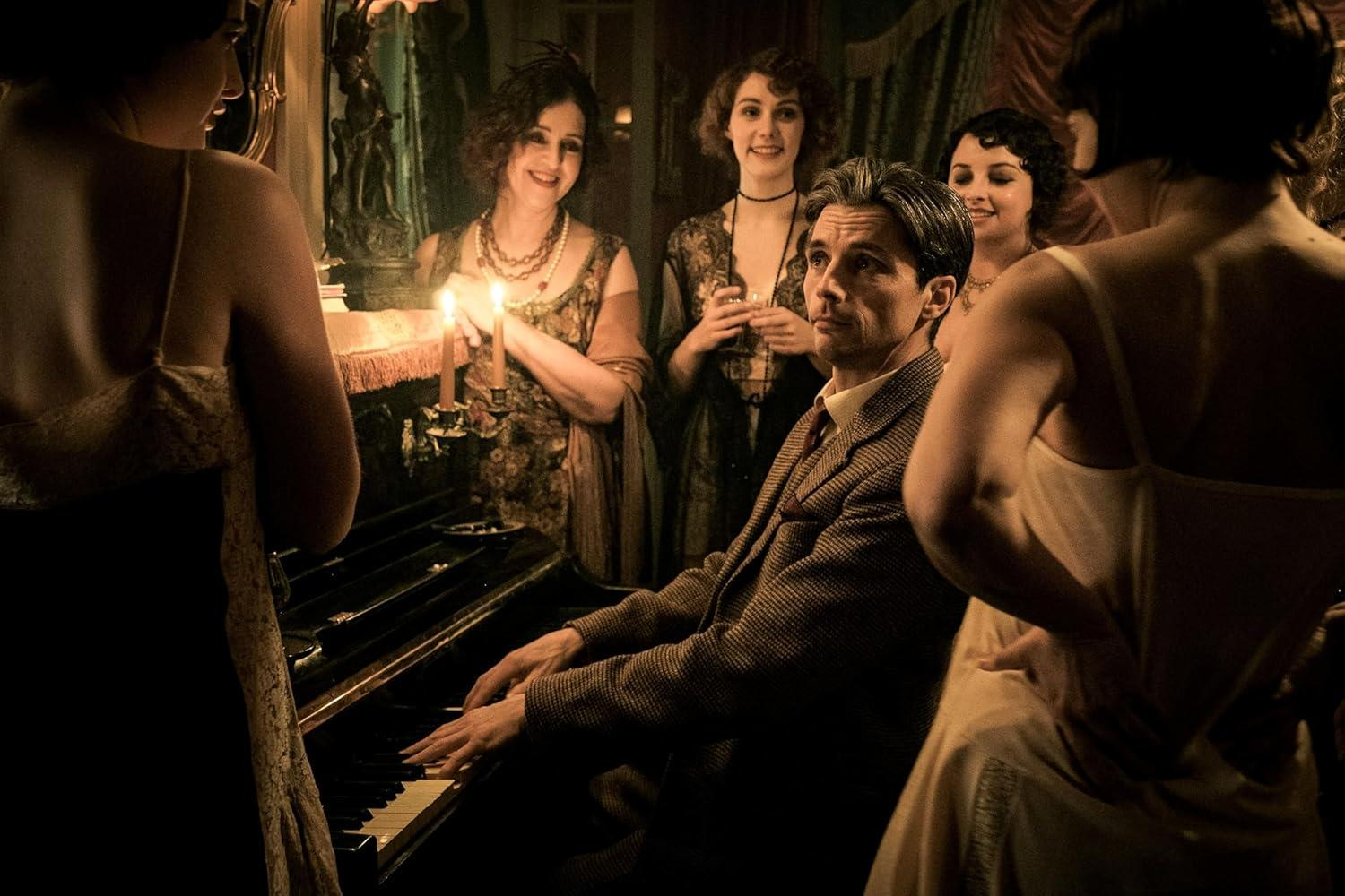 Ein Mann spielt Klavier, umgeben von Frauen in historischer Kleidung bei Kerzenlicht.