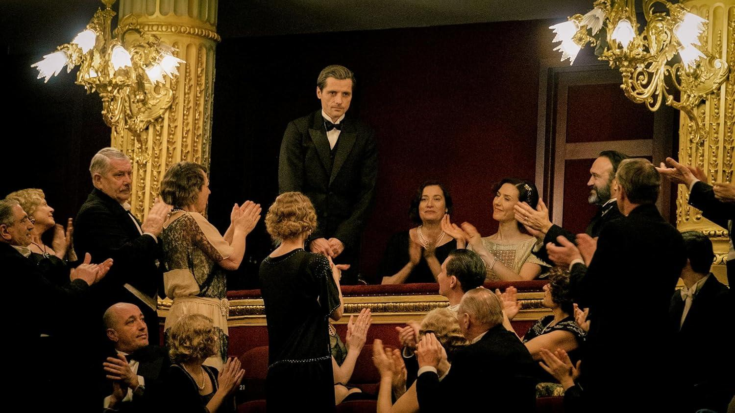 Eine Gruppe von Menschen applaudiert in einem opulenten Theater.