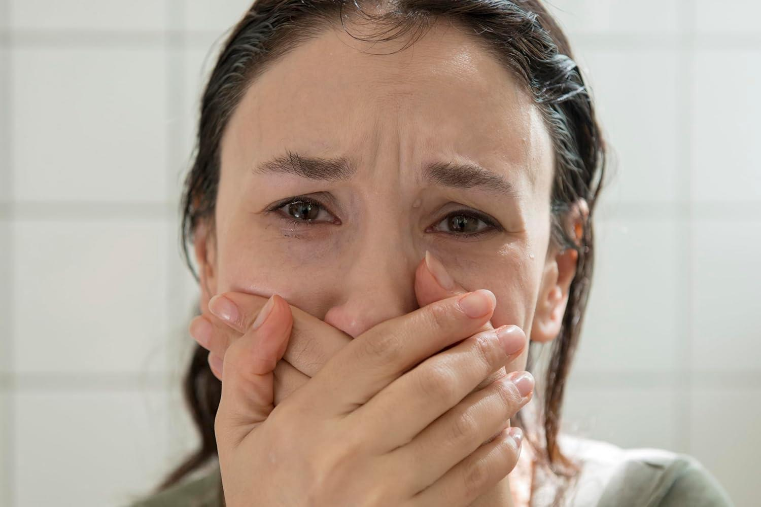 Eine Frau weint und bedeckt ihren Mund mit den Händen. Tränen laufen ihr übers Gesicht.