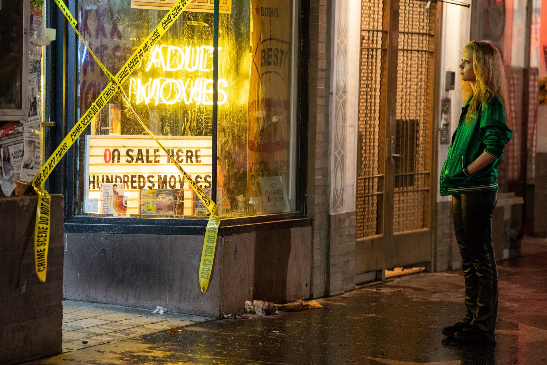 Eine Frau in grüner Jacke steht vor einem Kino mit gelbem Flatterband.