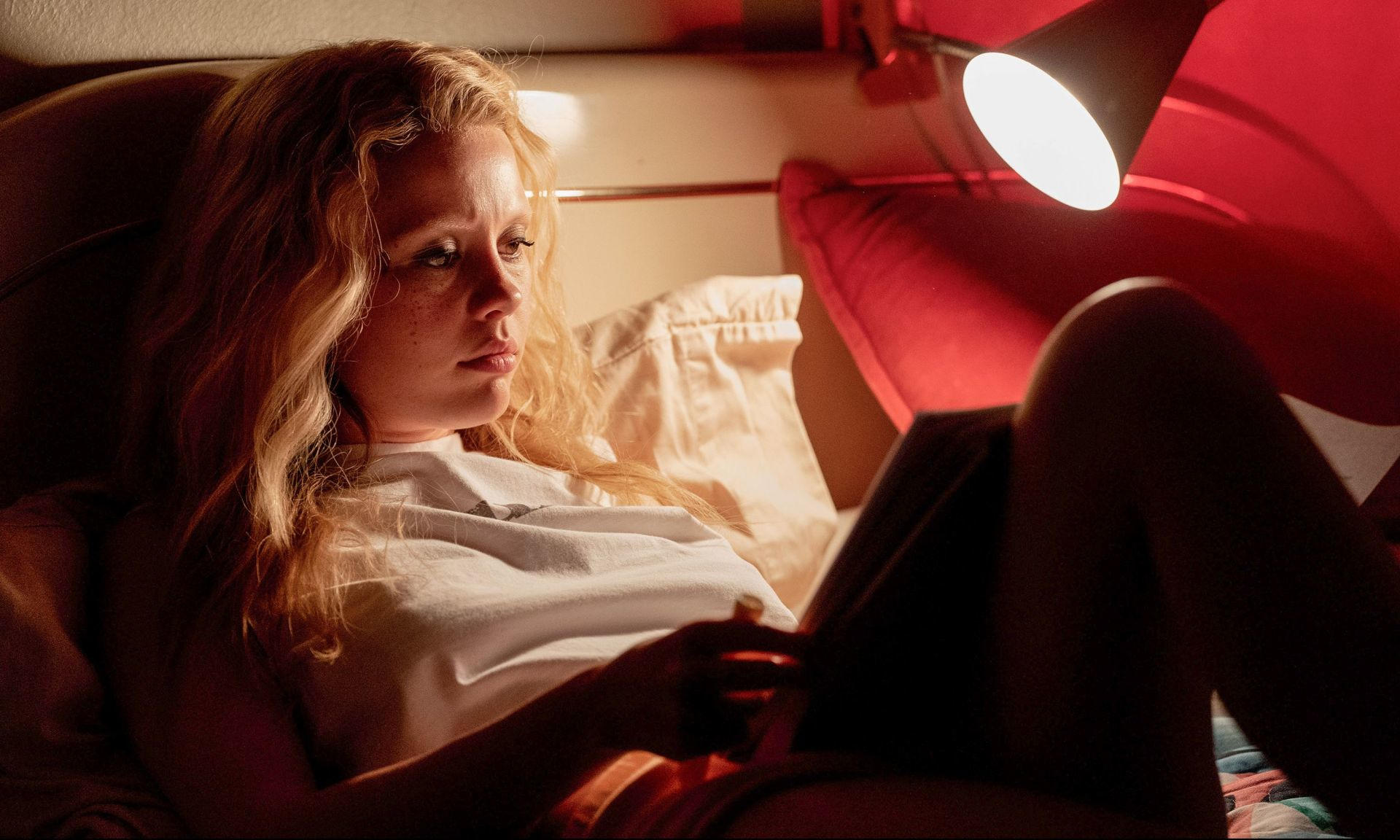 Eine junge Frau mit blonden Haaren liegt im Bett und liest.