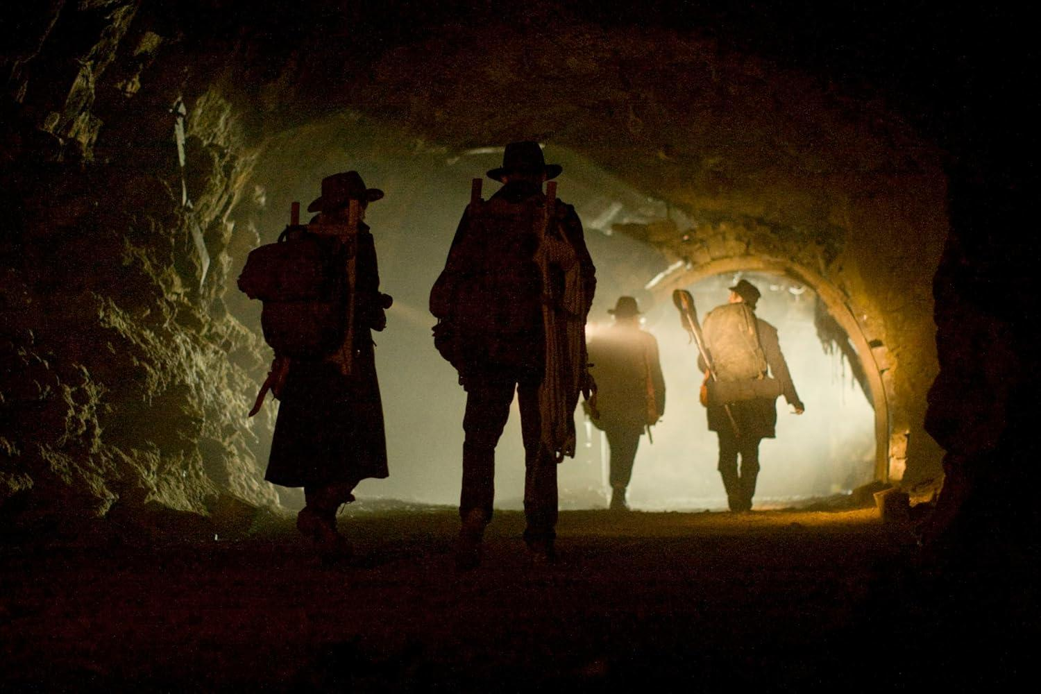 Vier Personen in Hüten und mit Rucksäcken gehen durch eine dunkle Höhle.