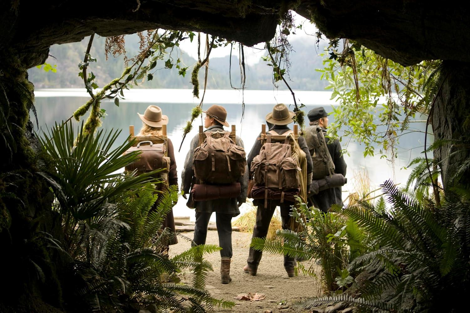 Vier Wanderer mit Rucksäcken blicken auf einen See von einer Höhle aus.