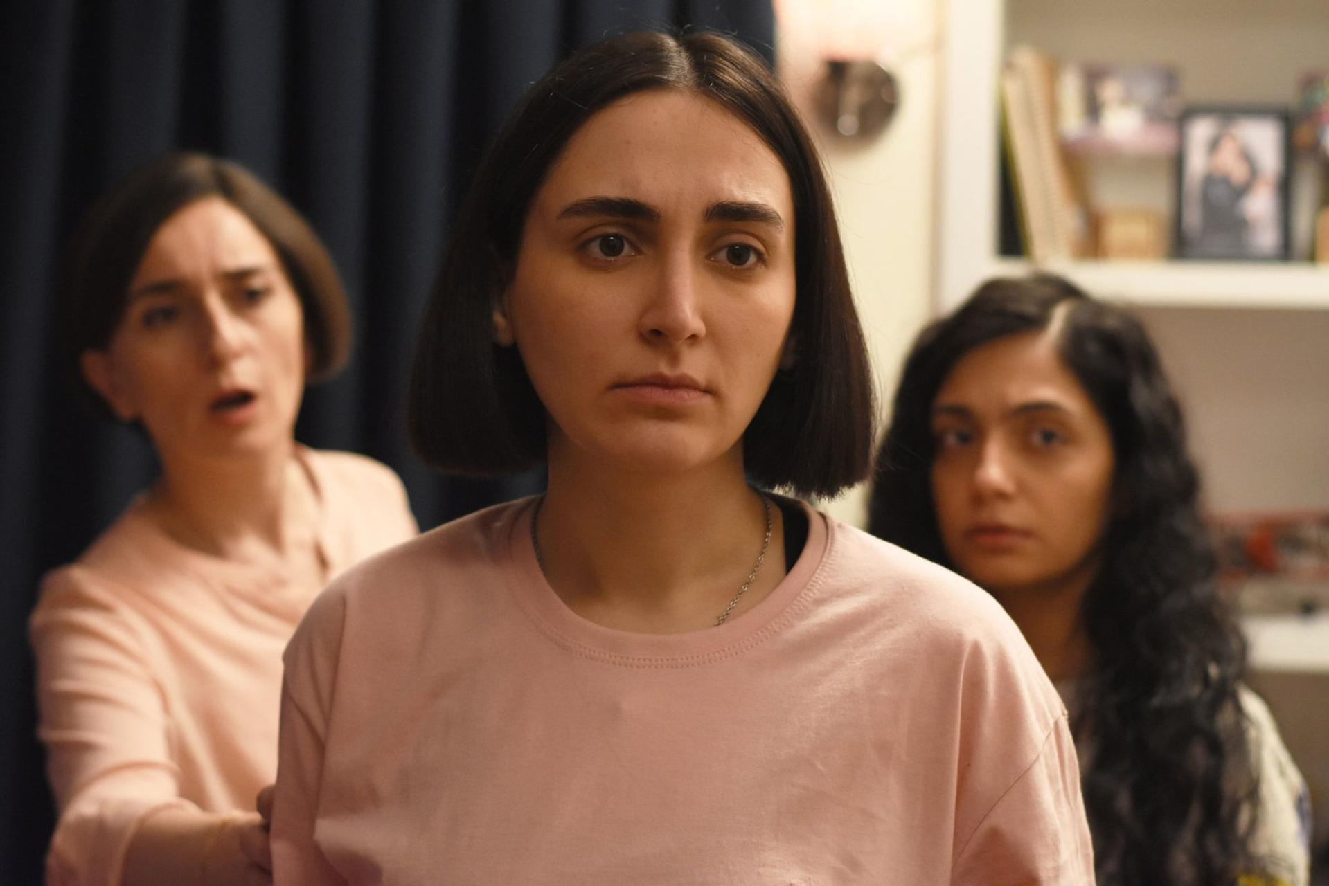 Drei Frauen in rosa Kleidung, zwei im Vordergrund, eine im Hintergrund.