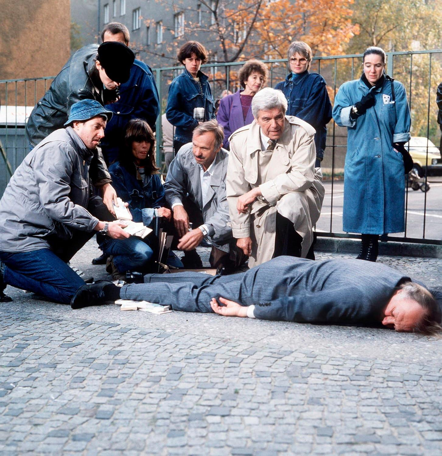 Polizeibeamte untersuchen eine leblose Person auf dem Boden, Geld liegt verstreut.