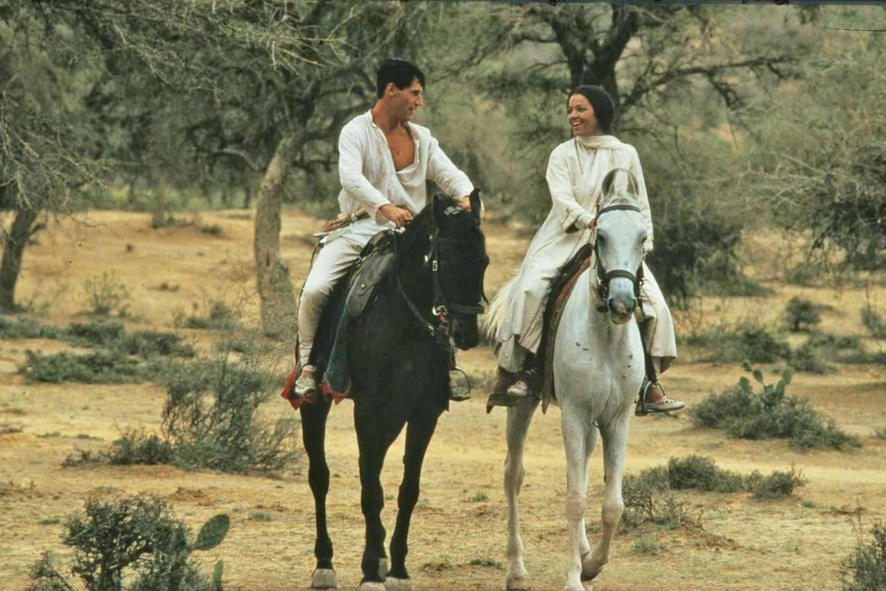 Mann und Frau reiten auf schwarzen und weißen Pferden in einer trockenen Landschaft.