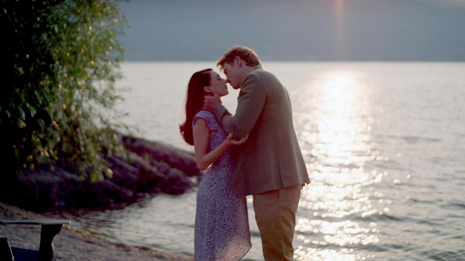 Ein Mann und eine Frau küssen sich am Ufer eines Sees bei Sonnenuntergang.