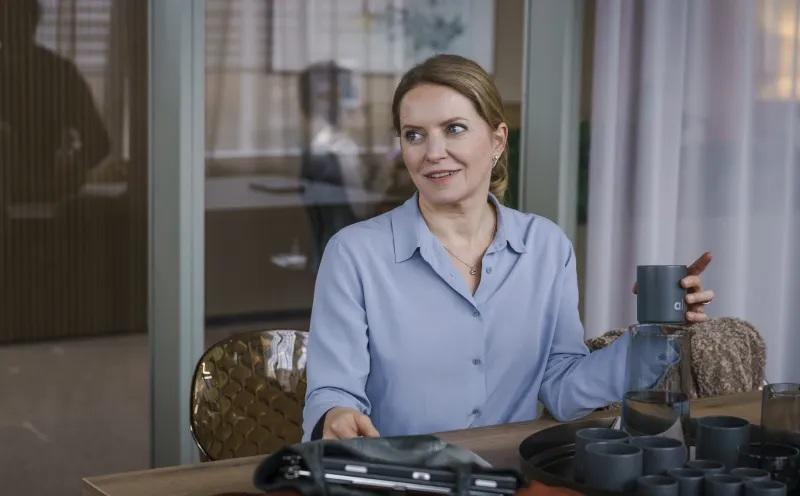 Eine Frau in einem blauen Hemd sitzt an einem Tisch und hält eine Tasse.