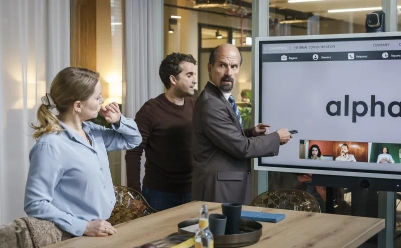 Männer und Frauen in einem Büro besprechen sich vor einem großen Bildschirm mit Videokonferenz. 