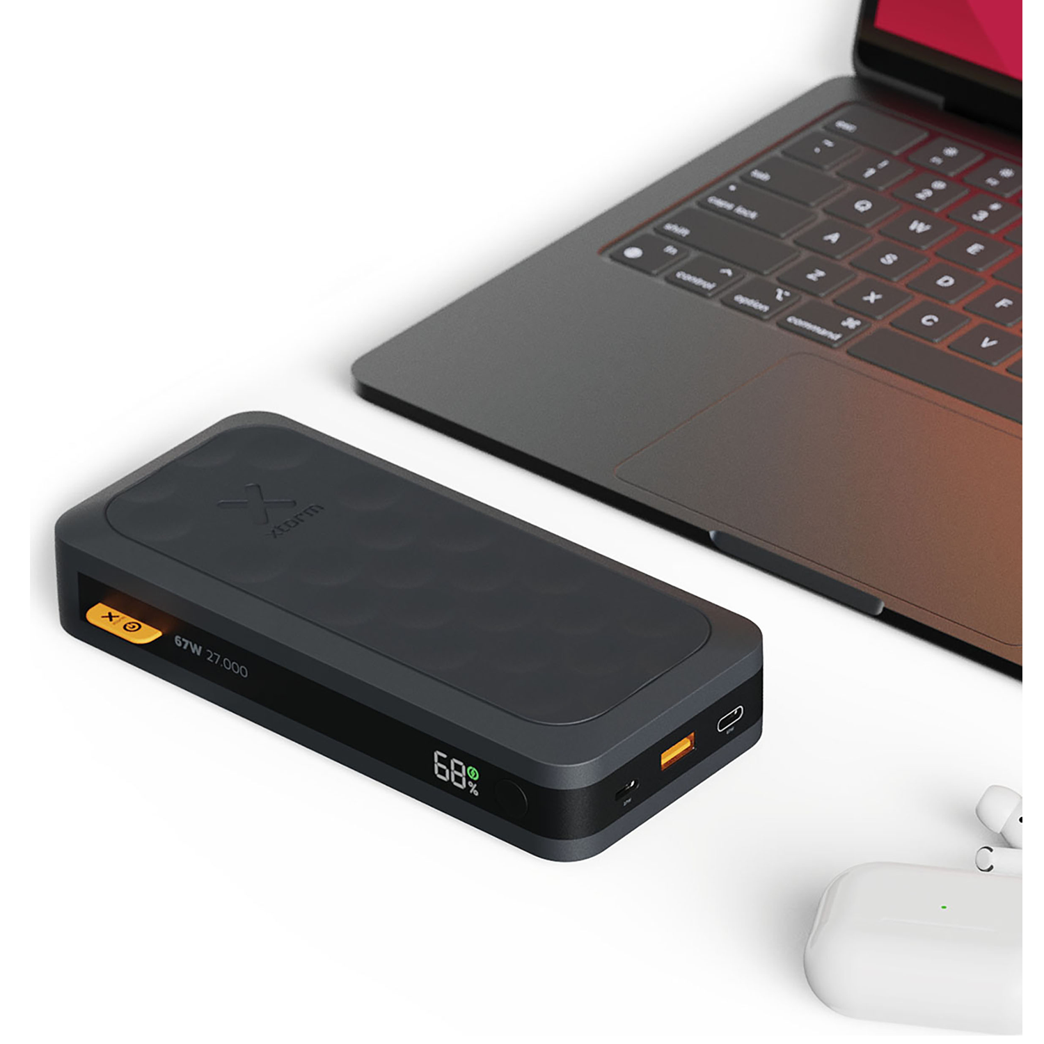 Zwarte powerbank naast laptop en witte oordopjes op witte ondergrond.