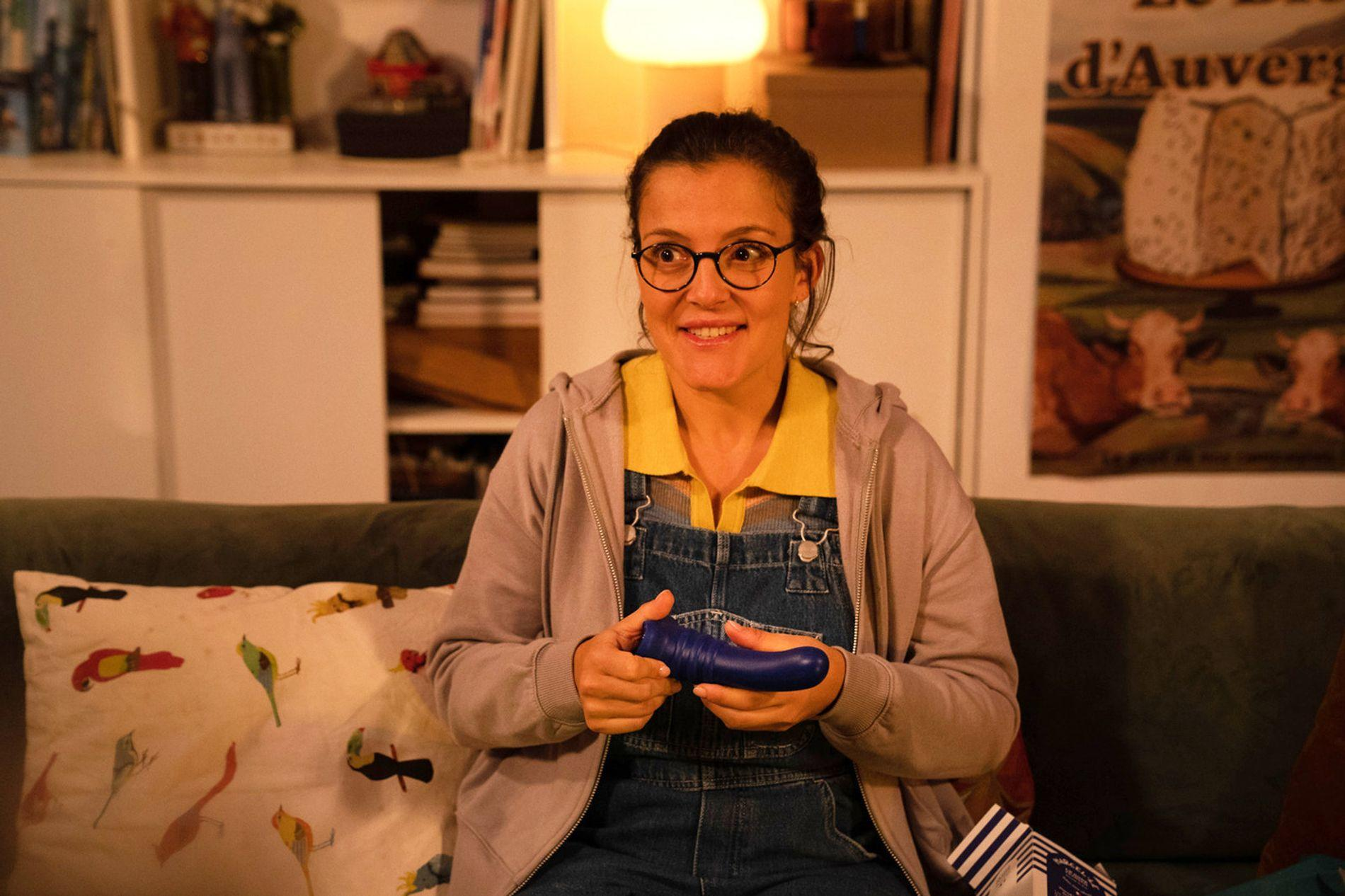 Eine Frau mit Brille sitzt auf einem Sofa und hält einen blauen Gegenstand.