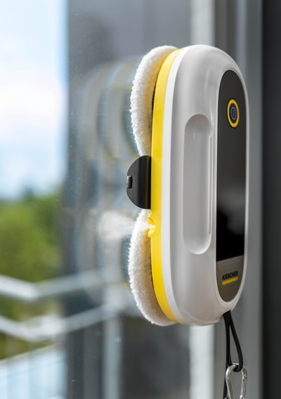 Biały robot do mycia okien z żółtym akcentem przyczepiony do okna.