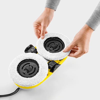 Ręce mocują białe szczotki do żółtej maszyny czyszczącej.