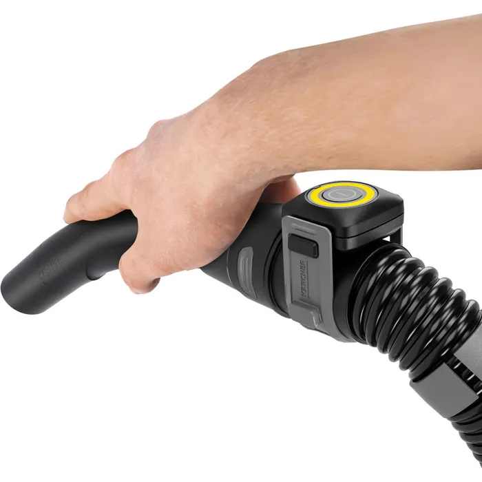 Ręka trzyma czarną rączkę odkurzacza z żółtym przyciskiem.