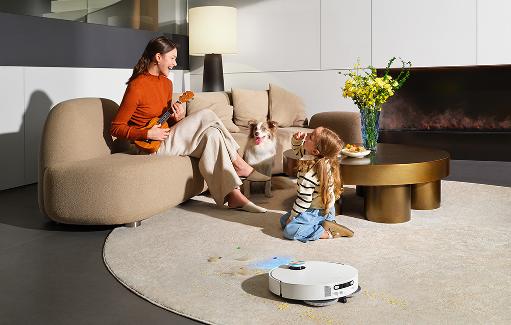 Kobieta gra na ukulele, dziecko karmi psa, robot sprzątający czyści dywan.