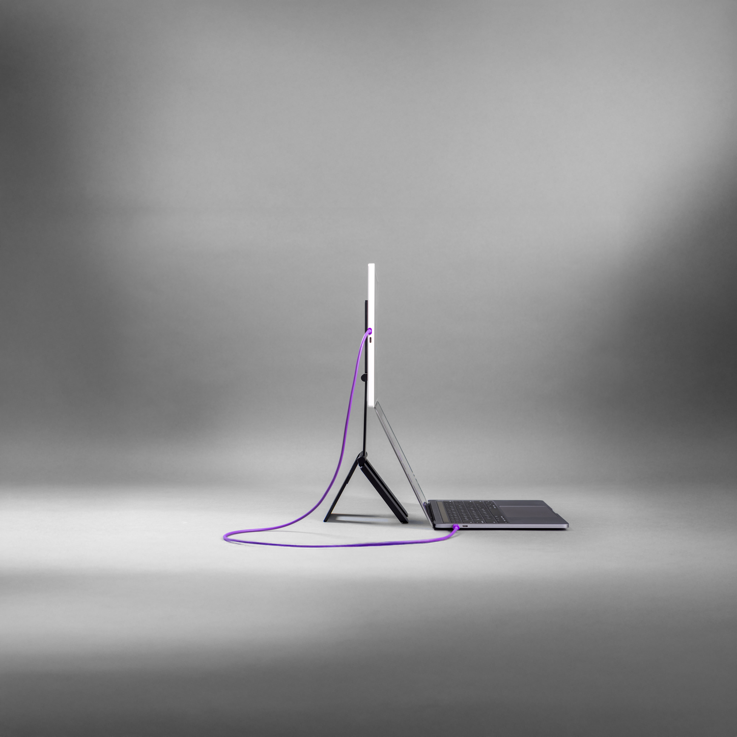 A dark laptop with a white screen and a purple cord connected to its back.