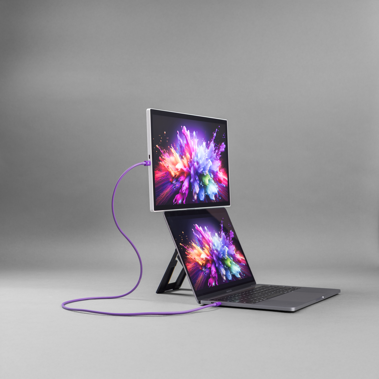 A laptop with an external monitor stacked on top, connected by a purple cable.