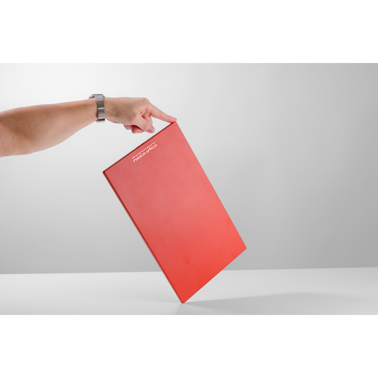 A hand wearing a silver watch holds a red notebook against a grey background.