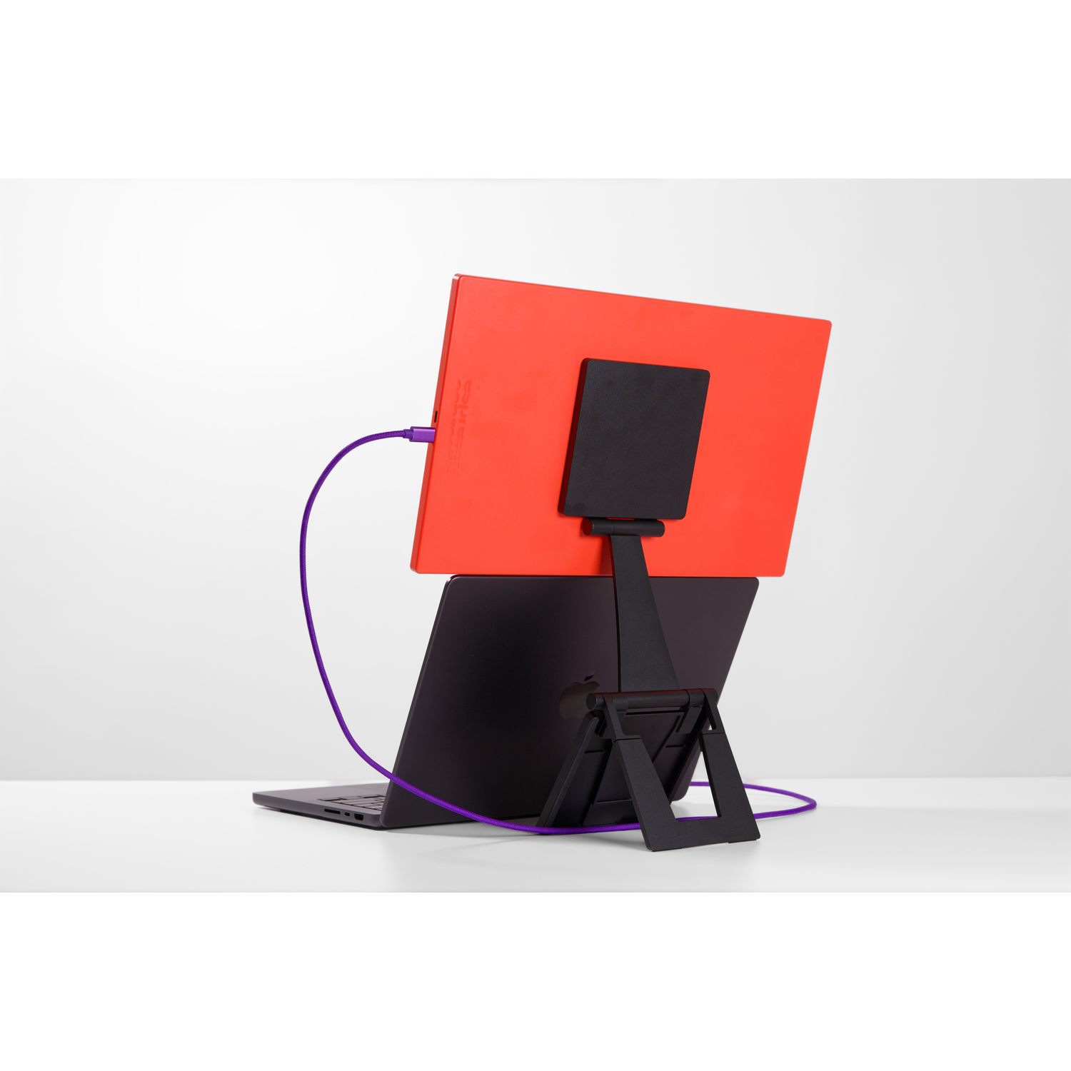 An orange screen is connected to a black laptop via a purple cable.