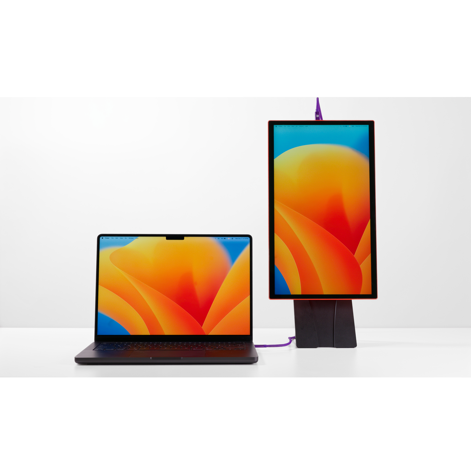 A laptop and a vertical monitor with orange and blue wallpapers on a white table.
