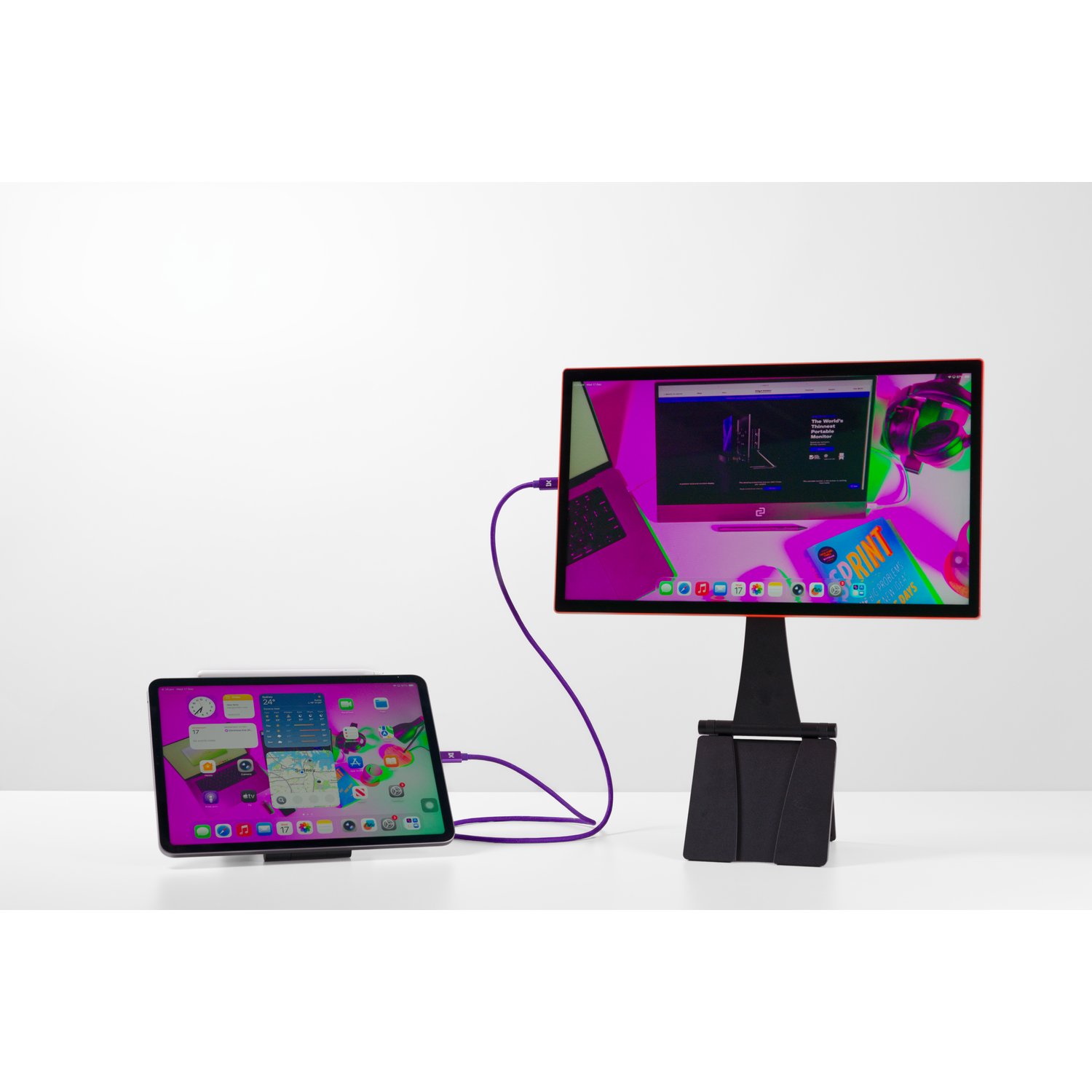 A tablet is connected to a monitor with a purple cable.