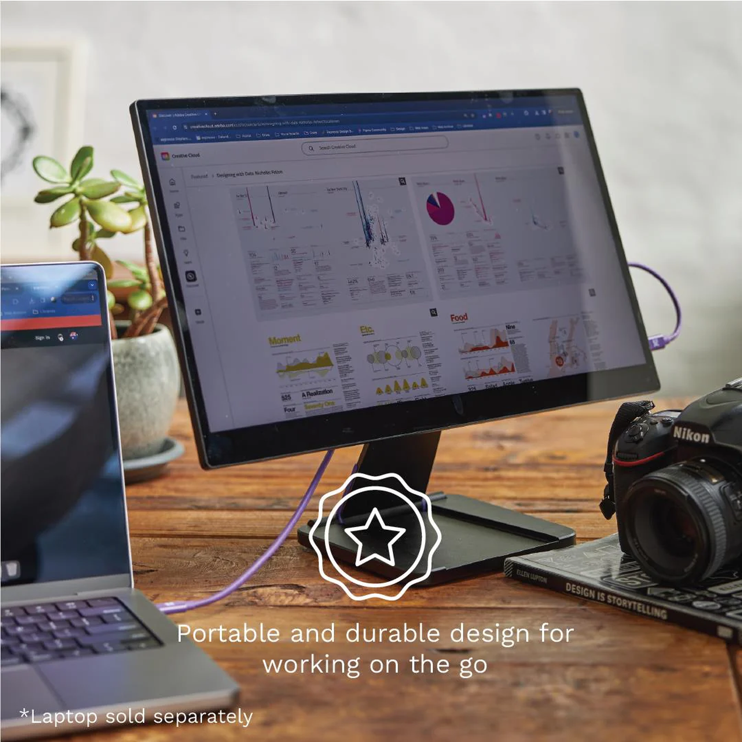Een laptop, monitor, camera en boek op een houten tafel.