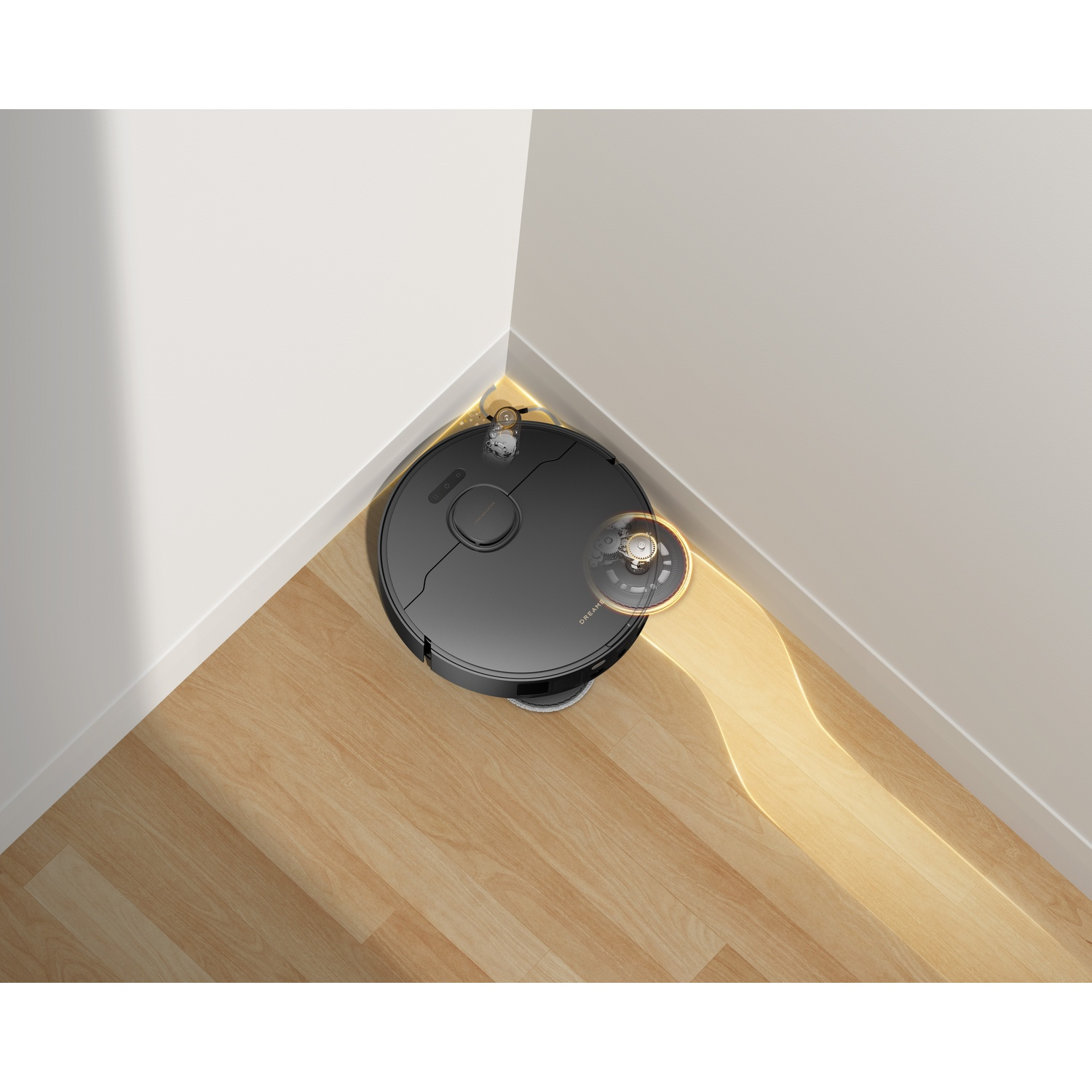 Un robot aspirapolvere nero pulisce un angolo di parquet con luce giallo-arancio.