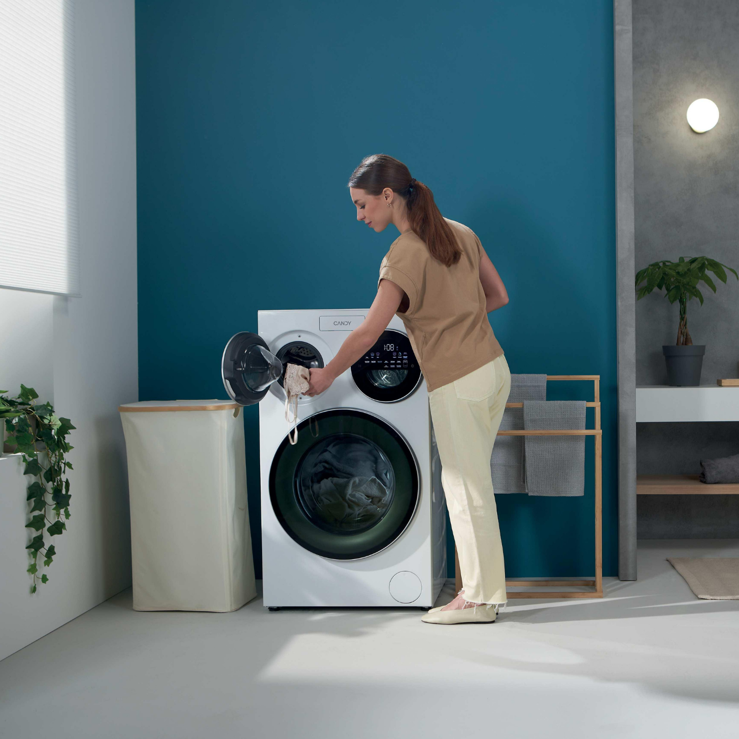 Una mujer carga ropa en una lavadora blanca en un baño moderno.