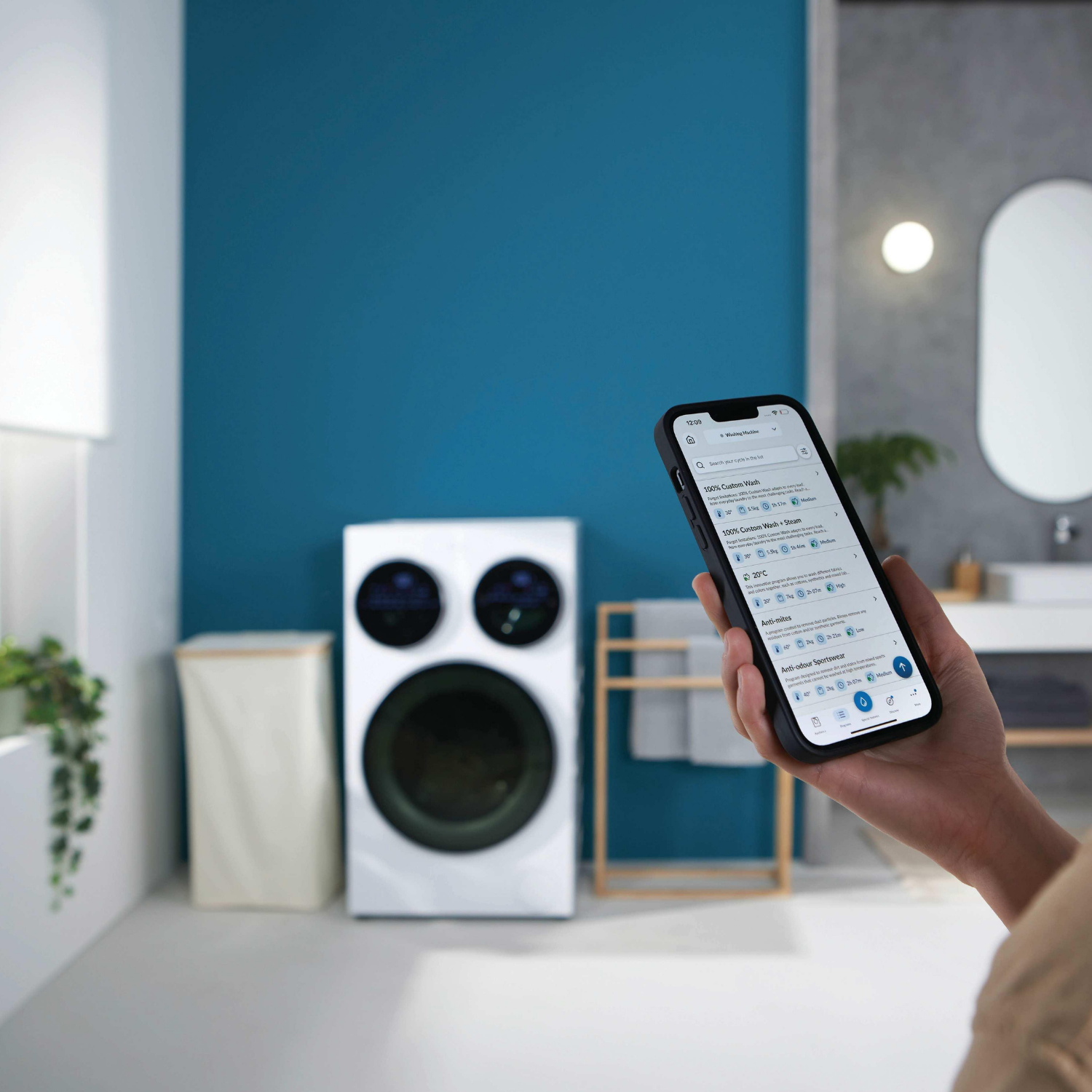 Una mano sostiene un smartphone con una app de lavadora frente a una lavadora.