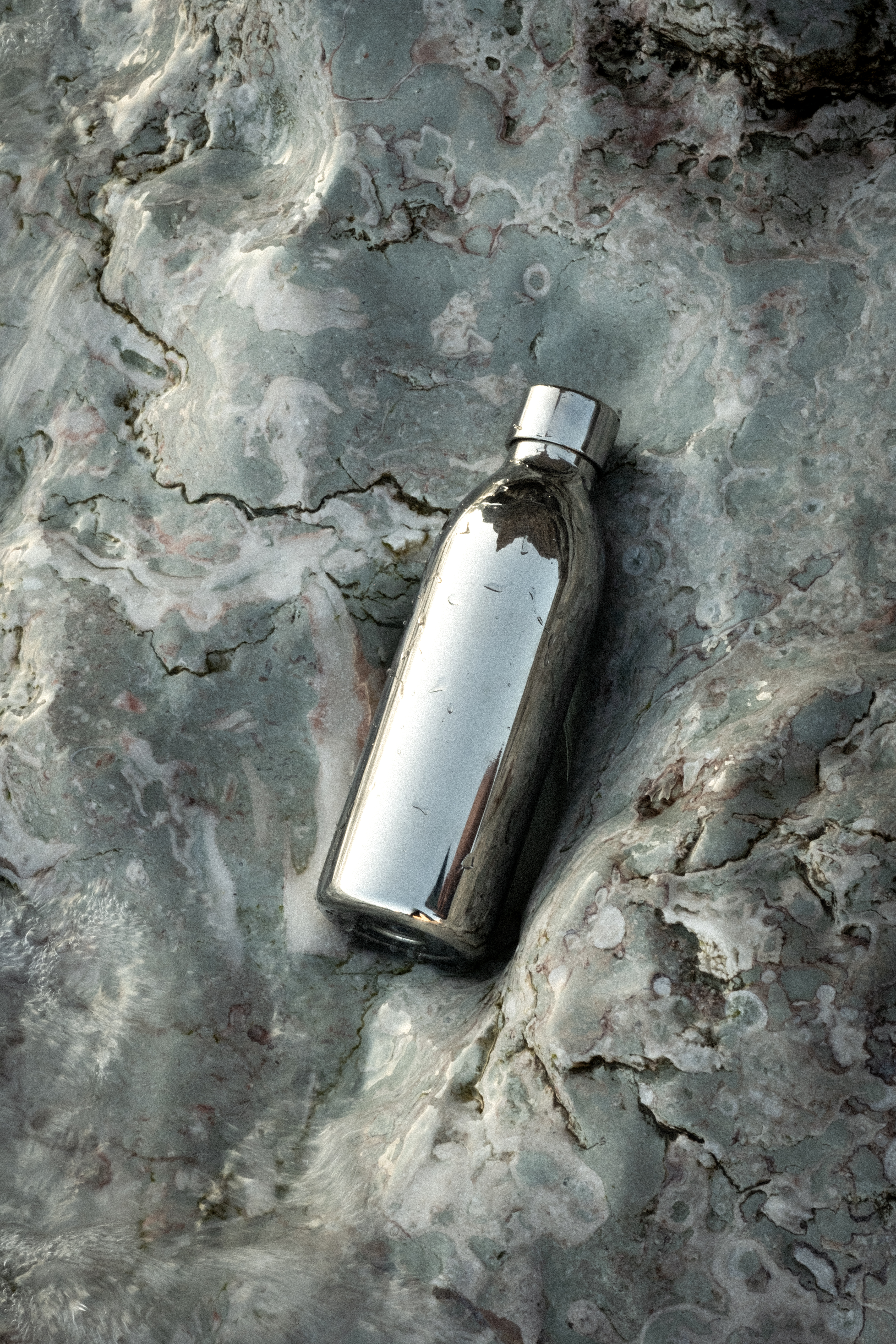 Eine glänzende silberne Flasche liegt auf einer strukturierten grauen Oberfläche.