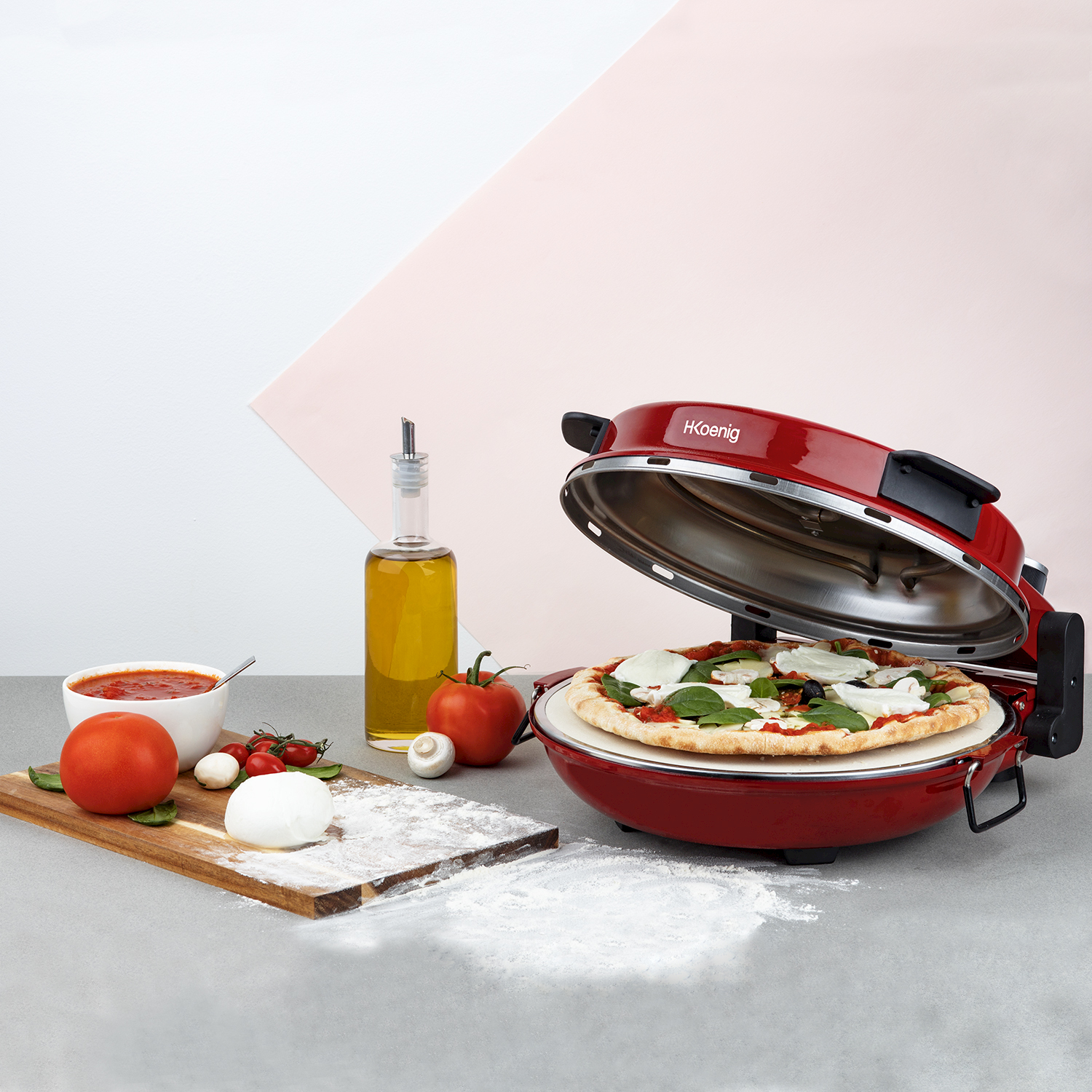 Forno per pizza rosso con pizza all'interno. Ingredienti come pomodori, mozzarella e olio d'oliva vicini.