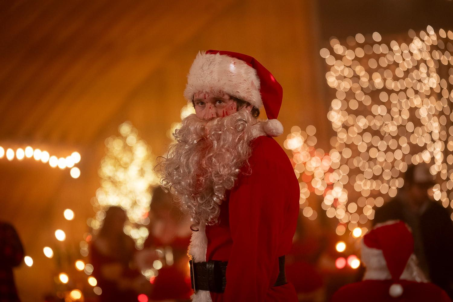 Ein Mann in einem blutbefleckten Weihnachtsmannkostüm steht vor Lichtern.