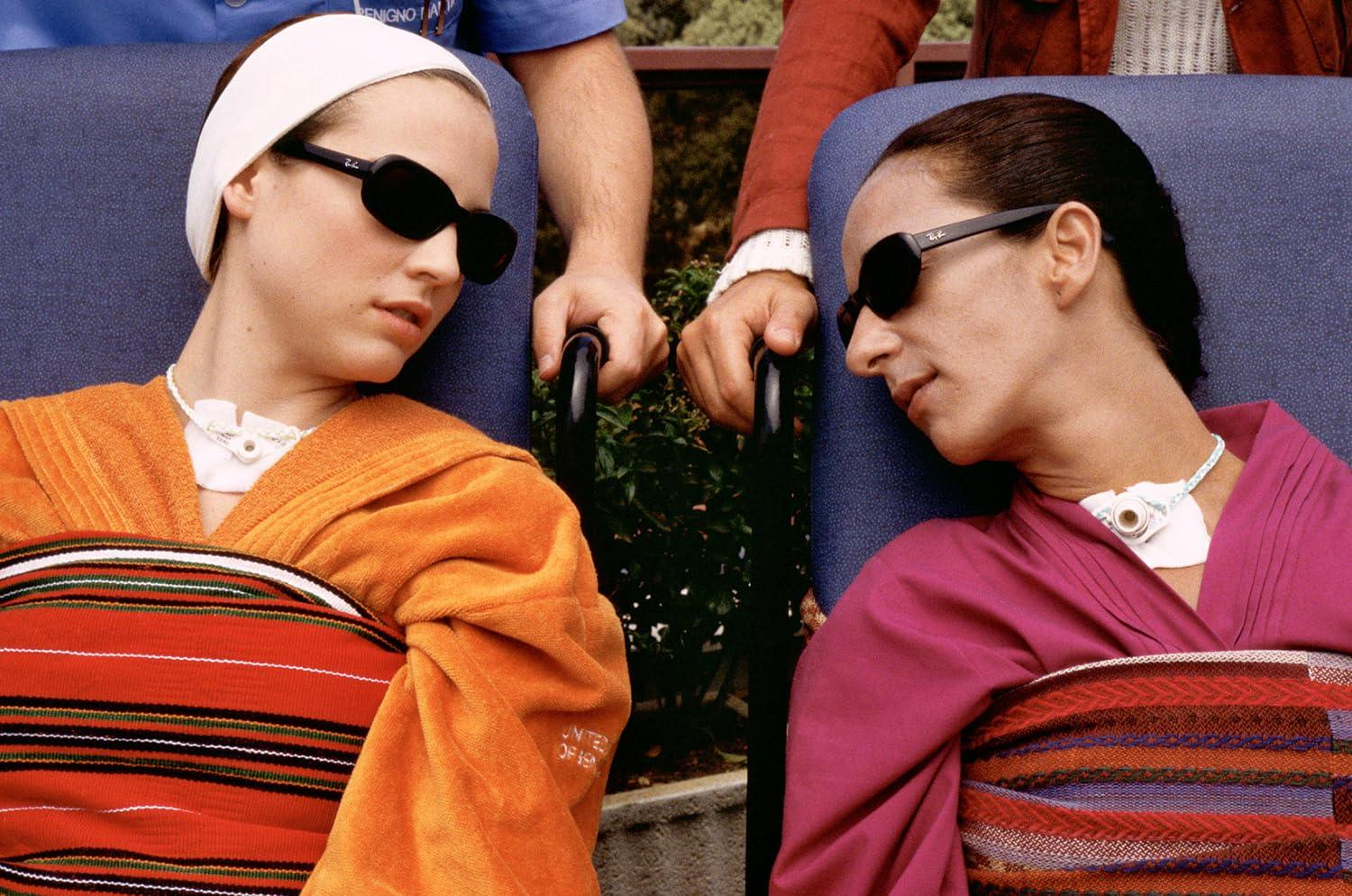 Zwei Frauen in Liegestühlen, eine in Orange, die andere in Pink, tragen Sonnenbrillen.