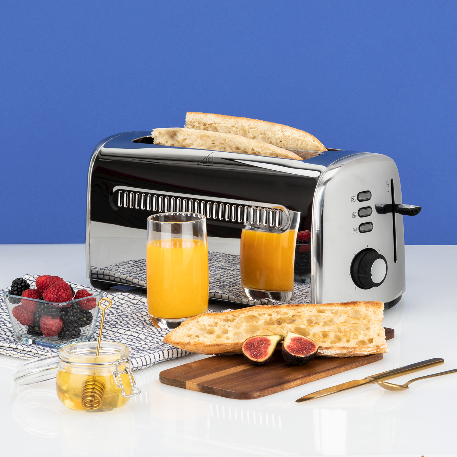 Un tostapane con pane, succo d'arancia, bacche e miele su un tavolo bianco.