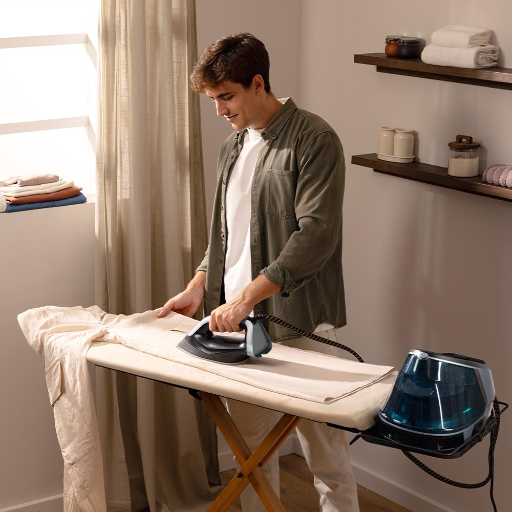 Hombre planchando ropa en tabla de planchar con plancha de vapor y depósito.