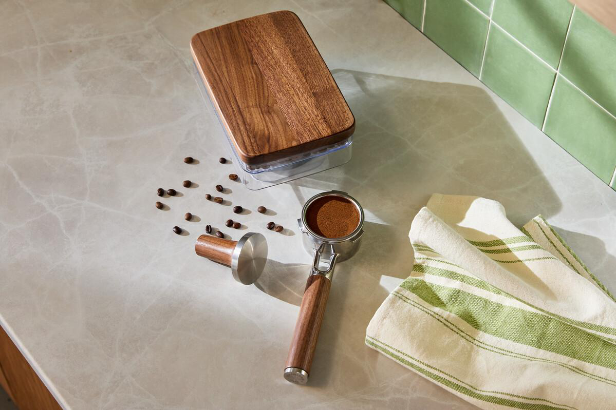 Espressomaschinenteil mit Kaffeepulver, Tamper, Bohnen und Tuch auf Marmor.