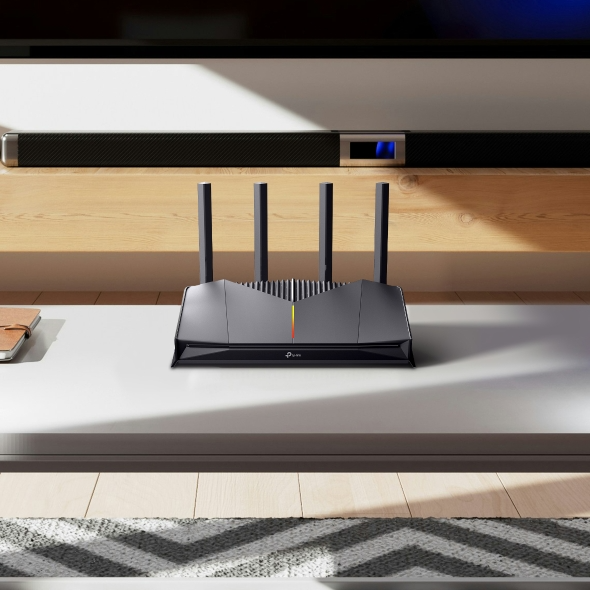 Egy fekete, négy antennás router áll egy fehér asztalon.