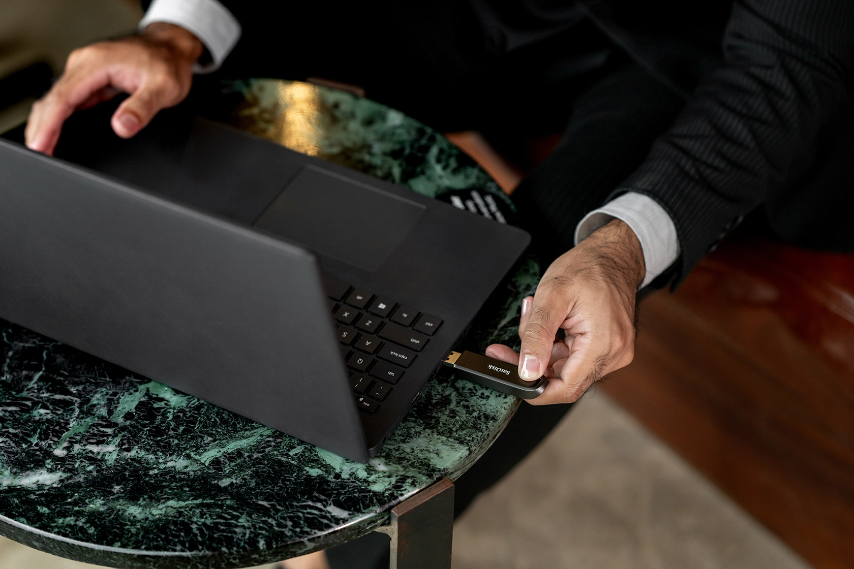 Mann steckt USB-Stick in schwarzen Laptop auf Marmortisch.