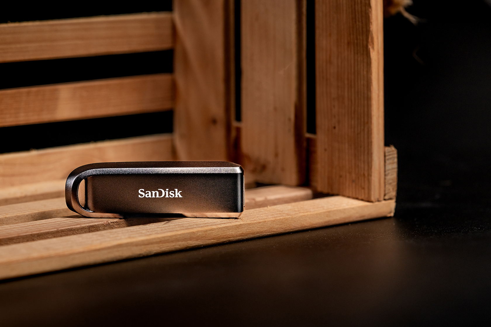 Ein dunkler SanDisk USB-Stick liegt auf Holzbalken in einer Holzkiste.