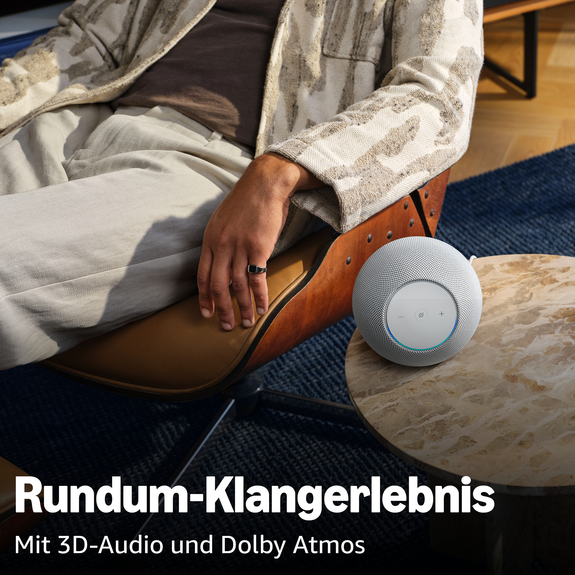 Ein Mann sitzt in einem Sessel neben einem runden Lautsprecher.