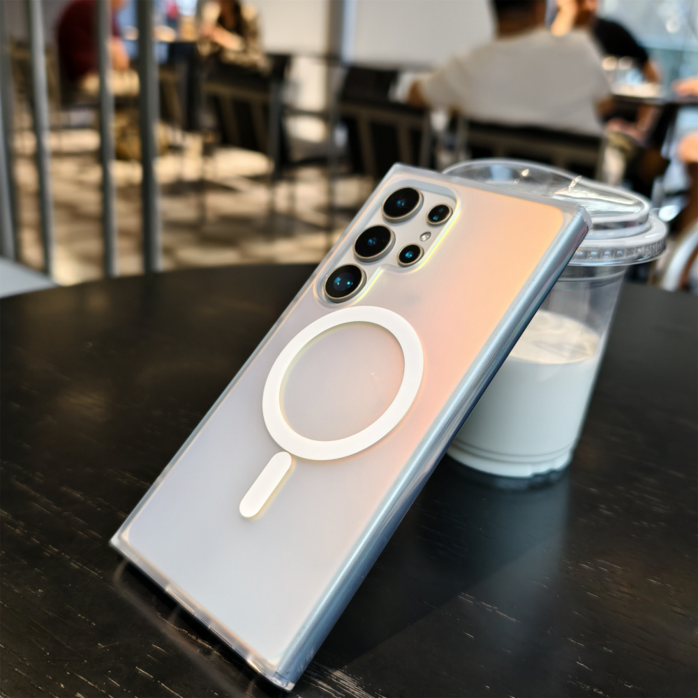 Egy MagSafe-es telefon átlátszó tokban egy pohár tej mellett.