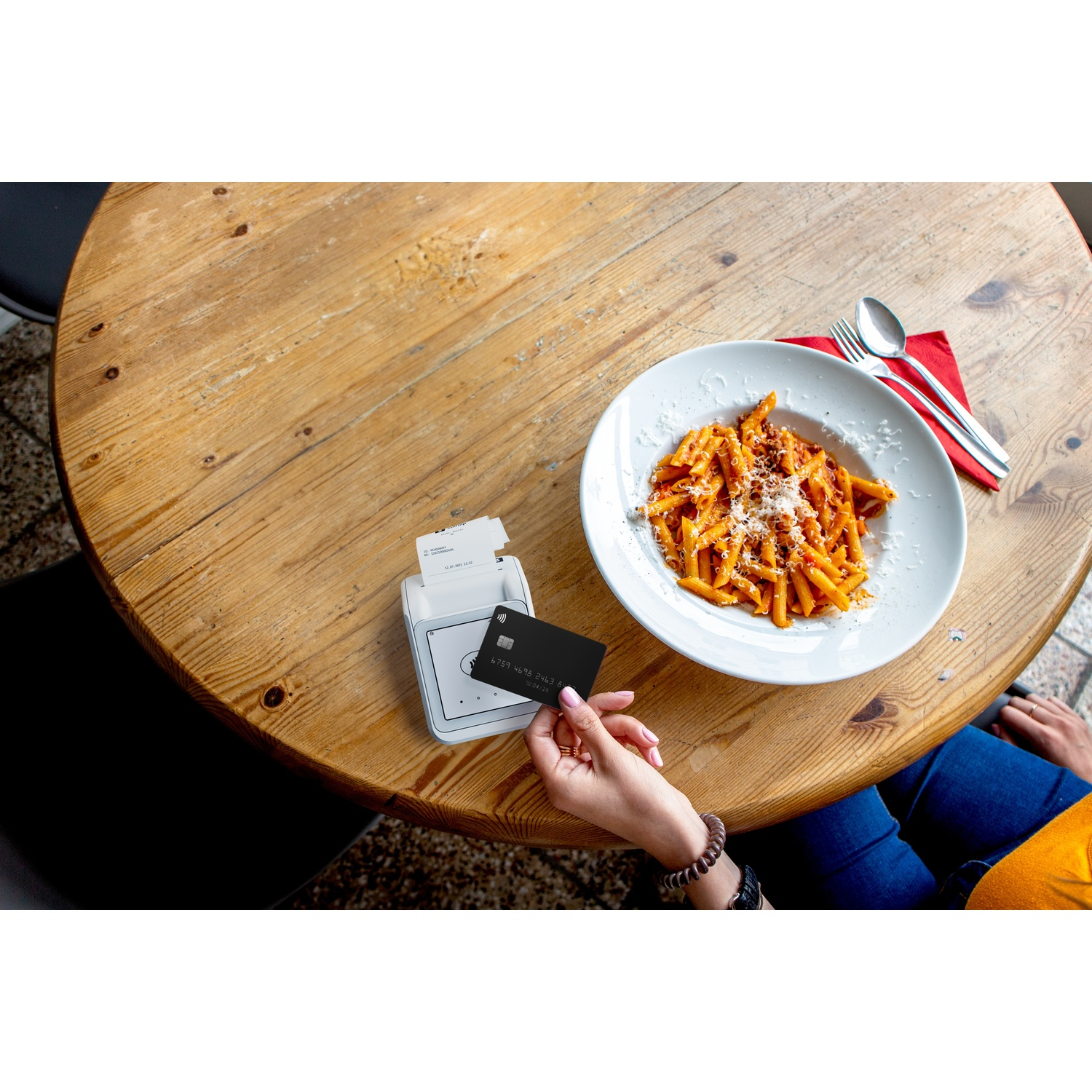 Una persona paga con carta nera a un terminal vicino a un piatto di pasta.