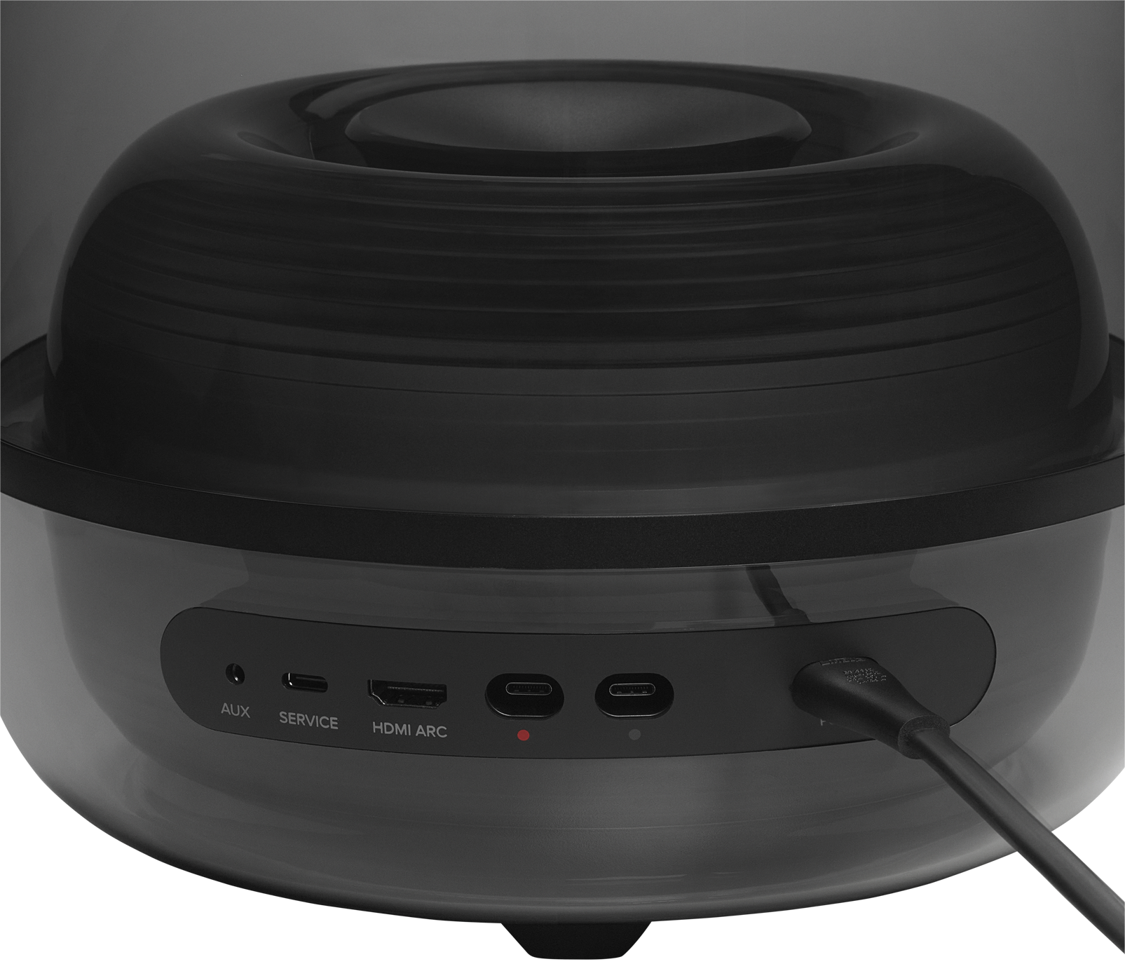 Fekete hangszóró portokkal: AUX, SERVICE, HDMI ARC és USB-C. Egy kábel be van dugva.