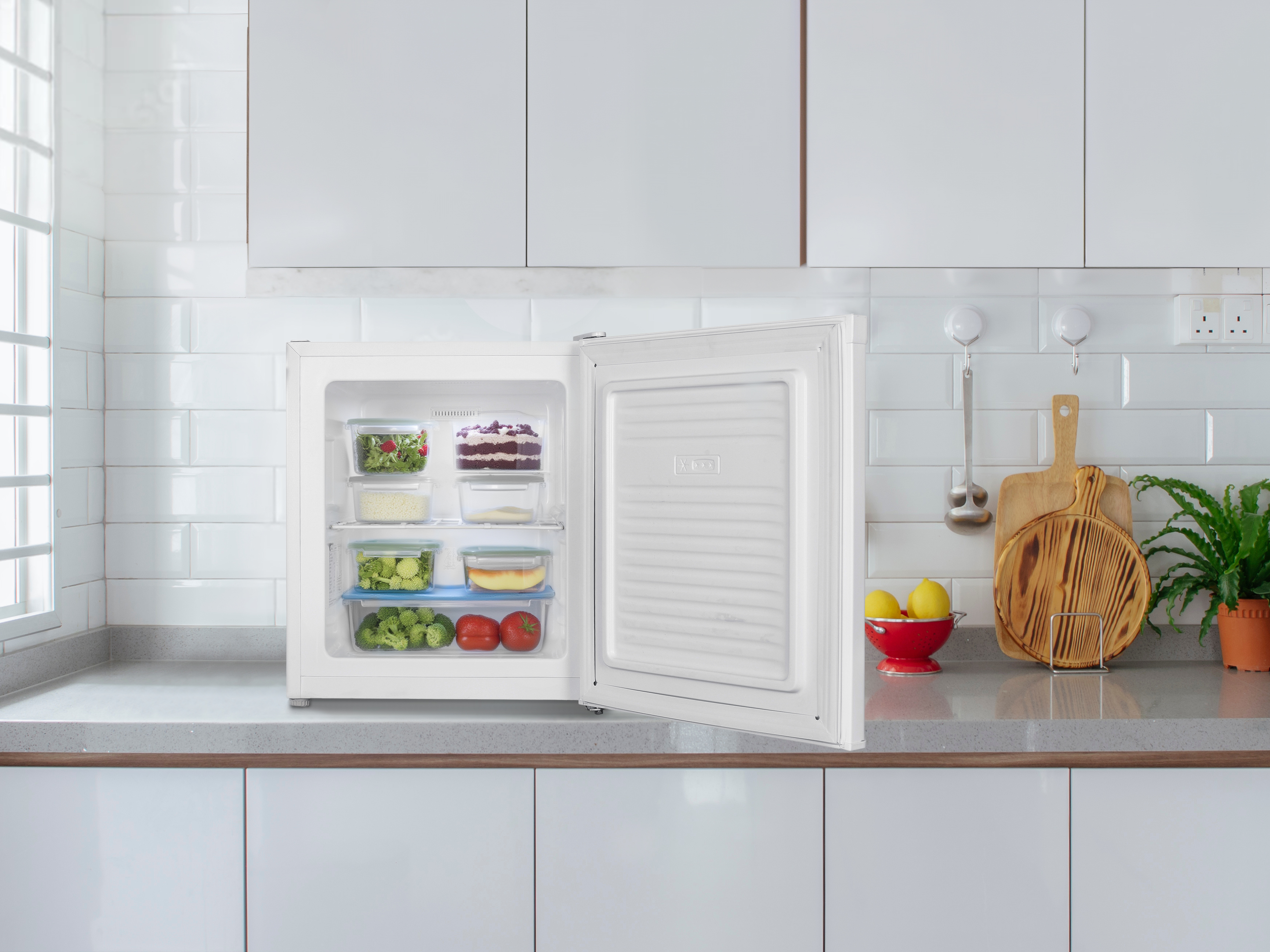 Offener weißer Kühlschrank mit Lebensmitteln und Kuchen, daneben Zitronen und Schneidebretter.
