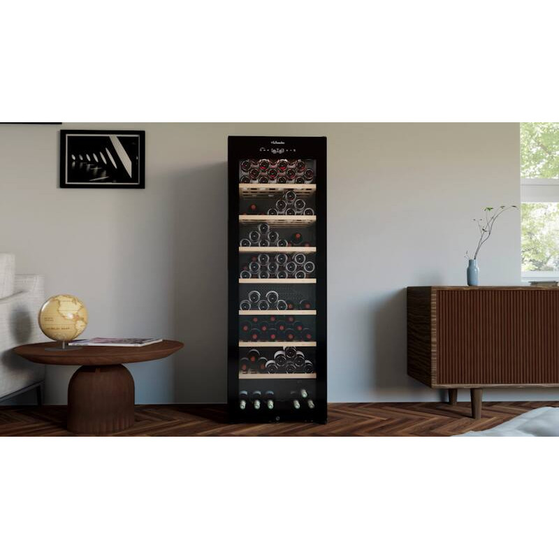 Ein schwarzer Weinkühlschrank mit vielen Flaschen auf Regalen, daneben ein runder Tisch.