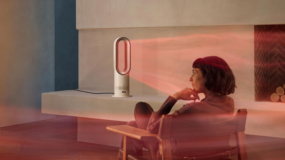 Une femme assise face à un radiateur soufflant émettant de la chaleur rouge.
