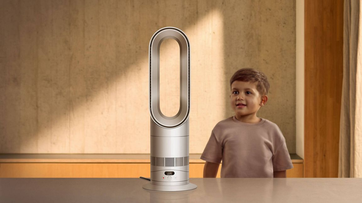Un garçon se tient à côté d'un ventilateur tour argenté sur une table.